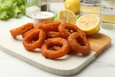 Photo of Fried squid rings served with sauce on white marble table, closeup