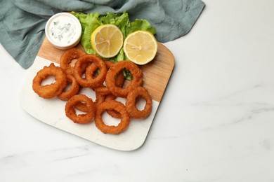 Photo of Fried squid rings served with sauce on white marble table, top view. Space for text