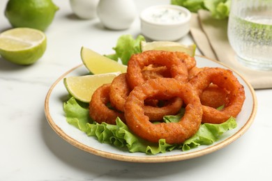 Photo of Fried squid rings served on white marble table, closeup