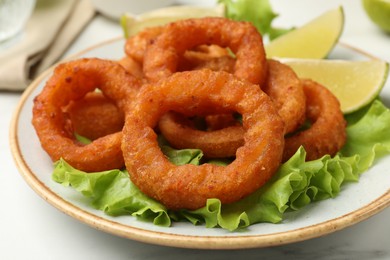 Photo of Fried squid rings, lime and lettuce on white marble table, closeup