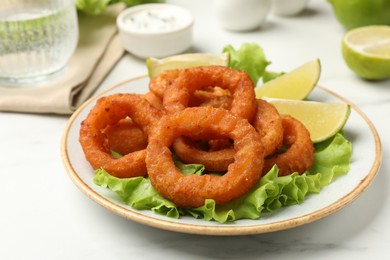 Photo of Fried squid rings served on white marble table, closeup
