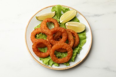 Photo of Fried squid rings, lime and lettuce on white marble table, top view