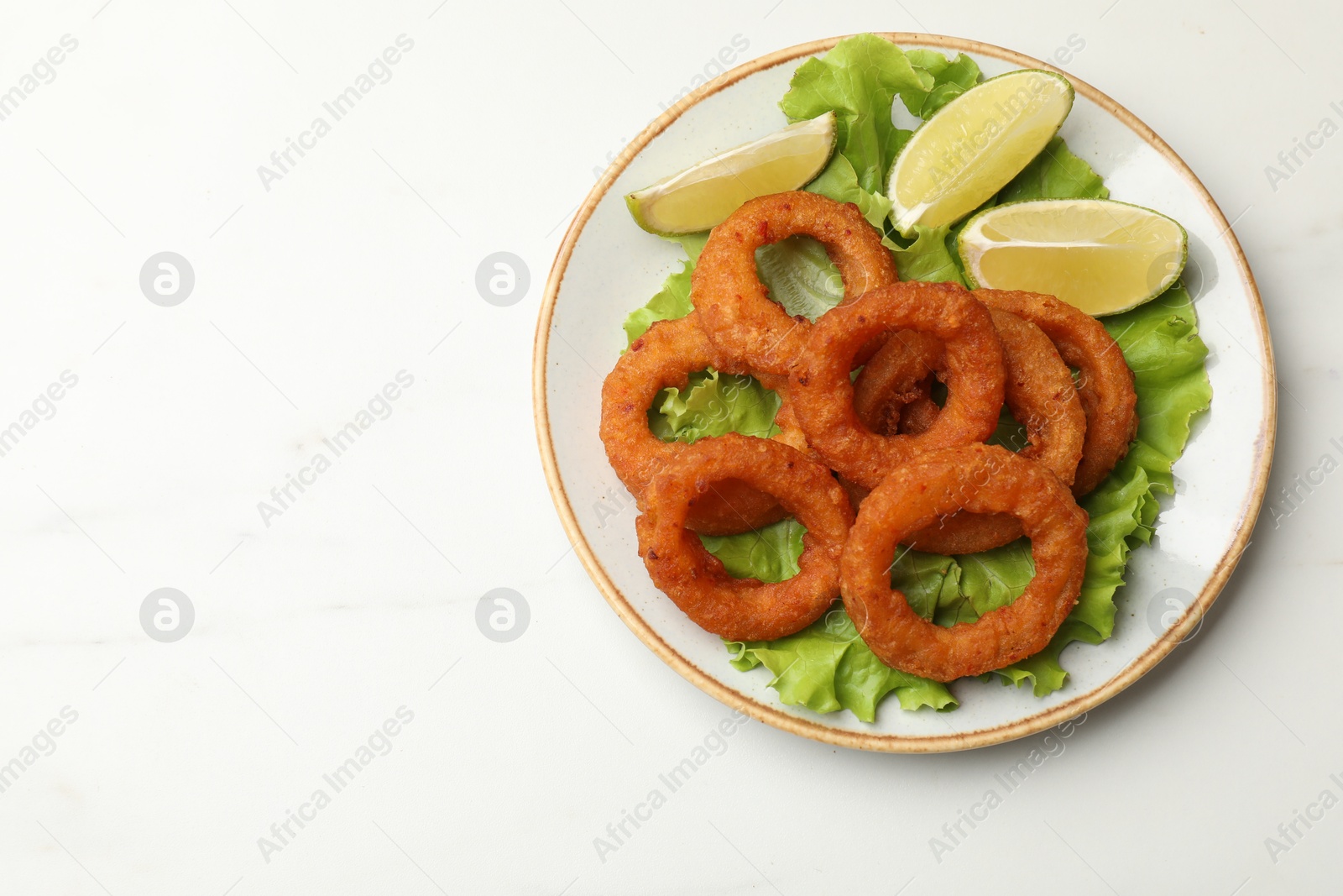 Fried squid rings, lime and lettuce on white marble table, top view. Space for text Photo of Fried squid rings, lime and lettuce on white marble table, top view. Space for text