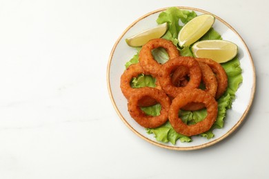 Photo of Fried squid rings, lime and lettuce on white marble table, top view. Space for text