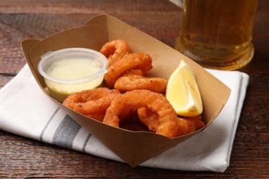 Photo of Fried squid rings, lemon, sauce and beer on wooden table, closeup
