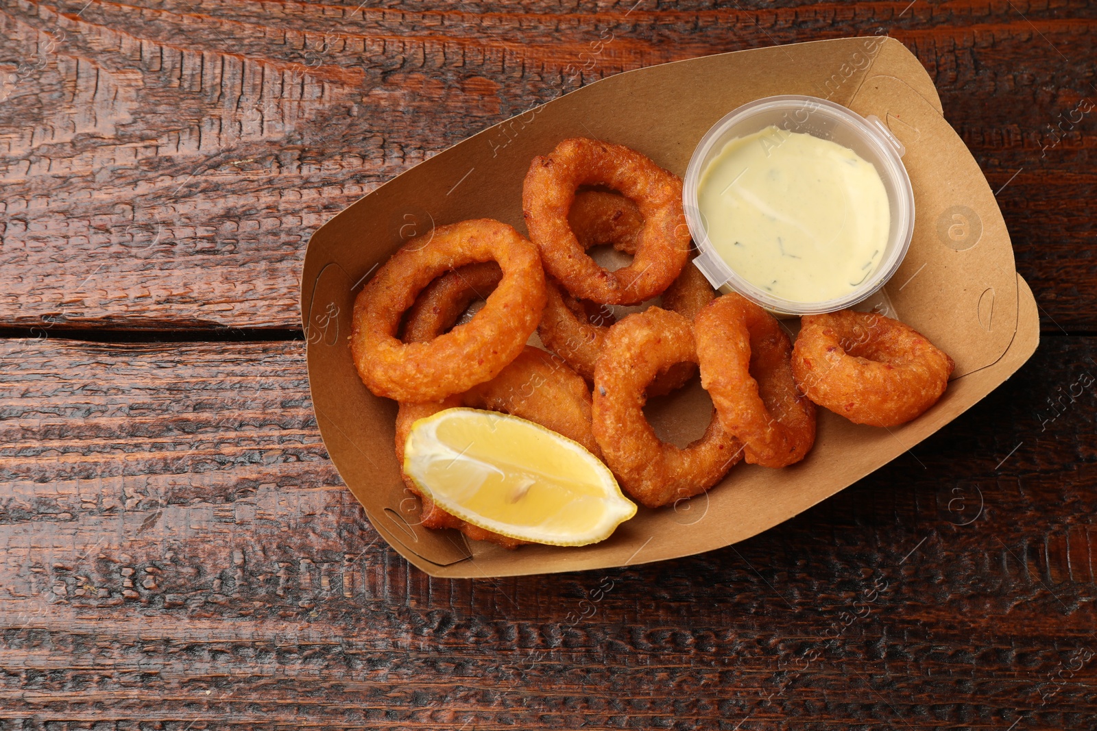 Fried squid rings, lemon and sauce on wooden table, top view. Space for text Photo of Fried squid rings, lemon and sauce on wooden table, top view. Space for text