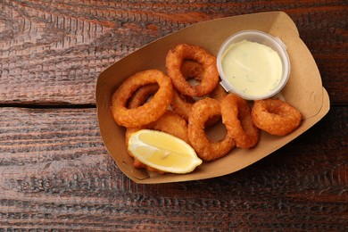 Photo of Fried squid rings, lemon and sauce on wooden table, top view. Space for text