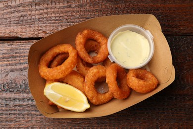 Photo of Fried squid rings, lemon and sauce on wooden table, top view