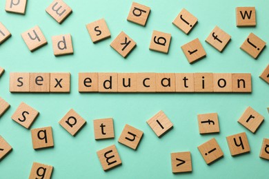 Photo of Words Sex Education made of wooden squares with letters on turquoise background, flat lay
