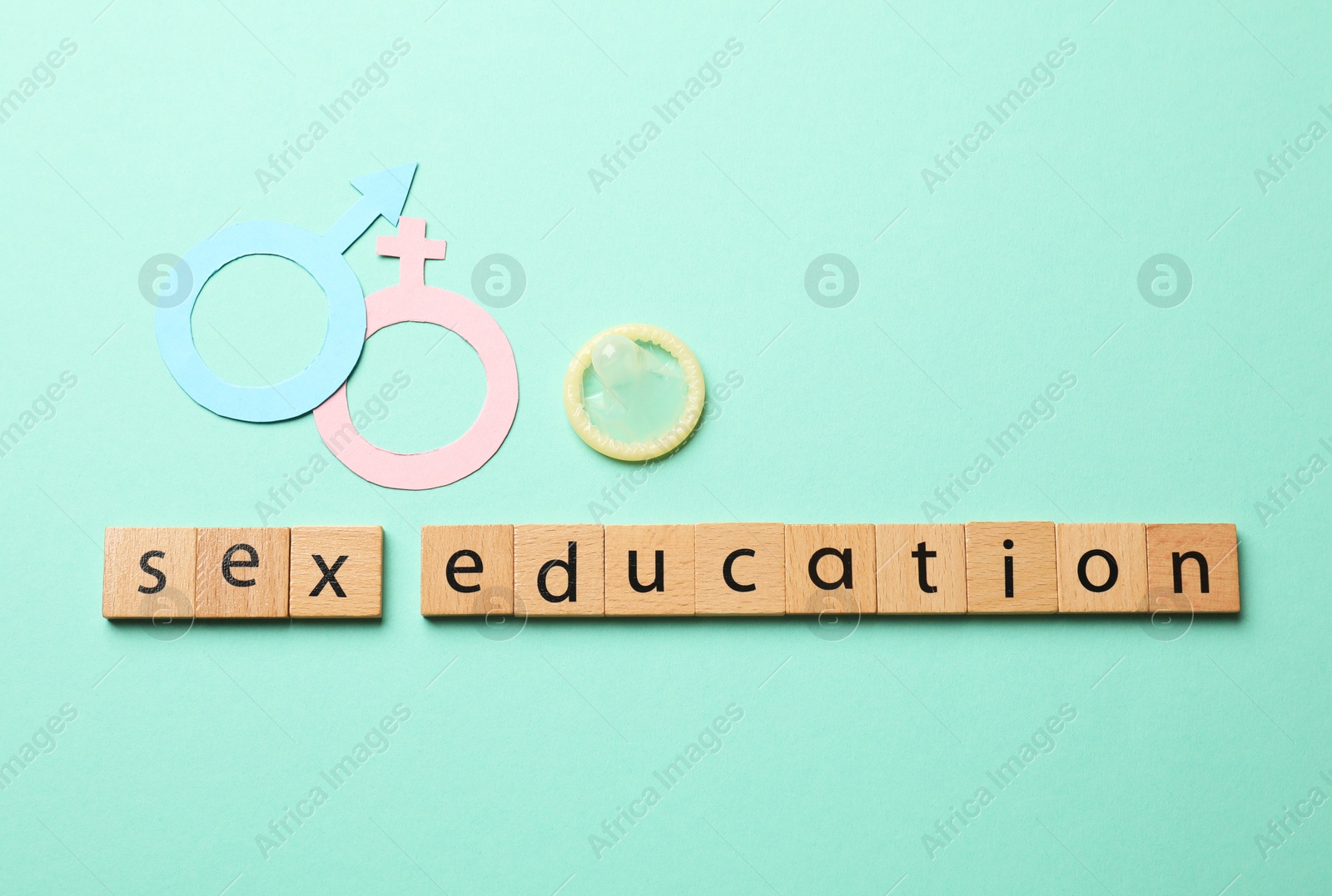 Photo of Words Sex Education made of wooden squares, gender symbols and condom on turquoise background, flat lay