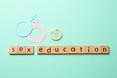 Photo of Words Sex Education made of wooden squares, gender symbols and condom on turquoise background, flat lay