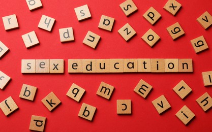 Photo of Words Sex Education made of wooden squares with letters on red background, flat lay