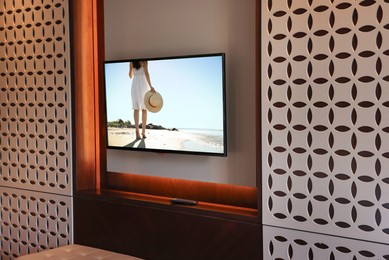 Image of TV set mounted on wall in room. Woman walking near sea on screen