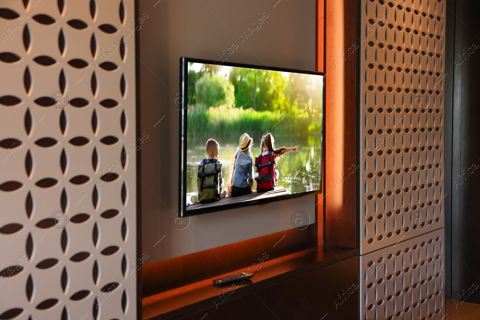 Image of TV set mounted on wall in room. Kids near river on screen