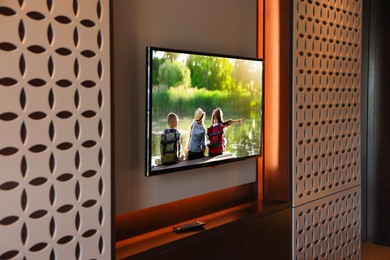 Image of TV set mounted on wall in room. Kids near river on screen