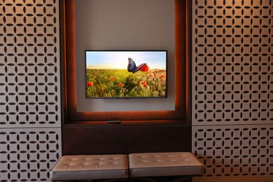Image of TV set mounted on wall in room. Flowers and butterfly on screen