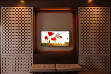 Image of TV set mounted on wall in room. Flowers and butterfly on screen