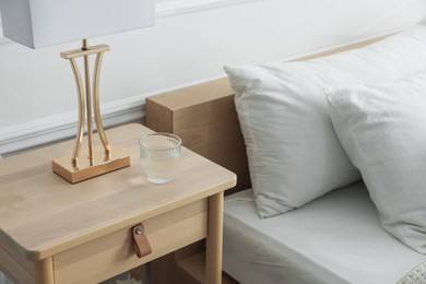 Photo of Bedside table with lamp and glass of water near bed indoors