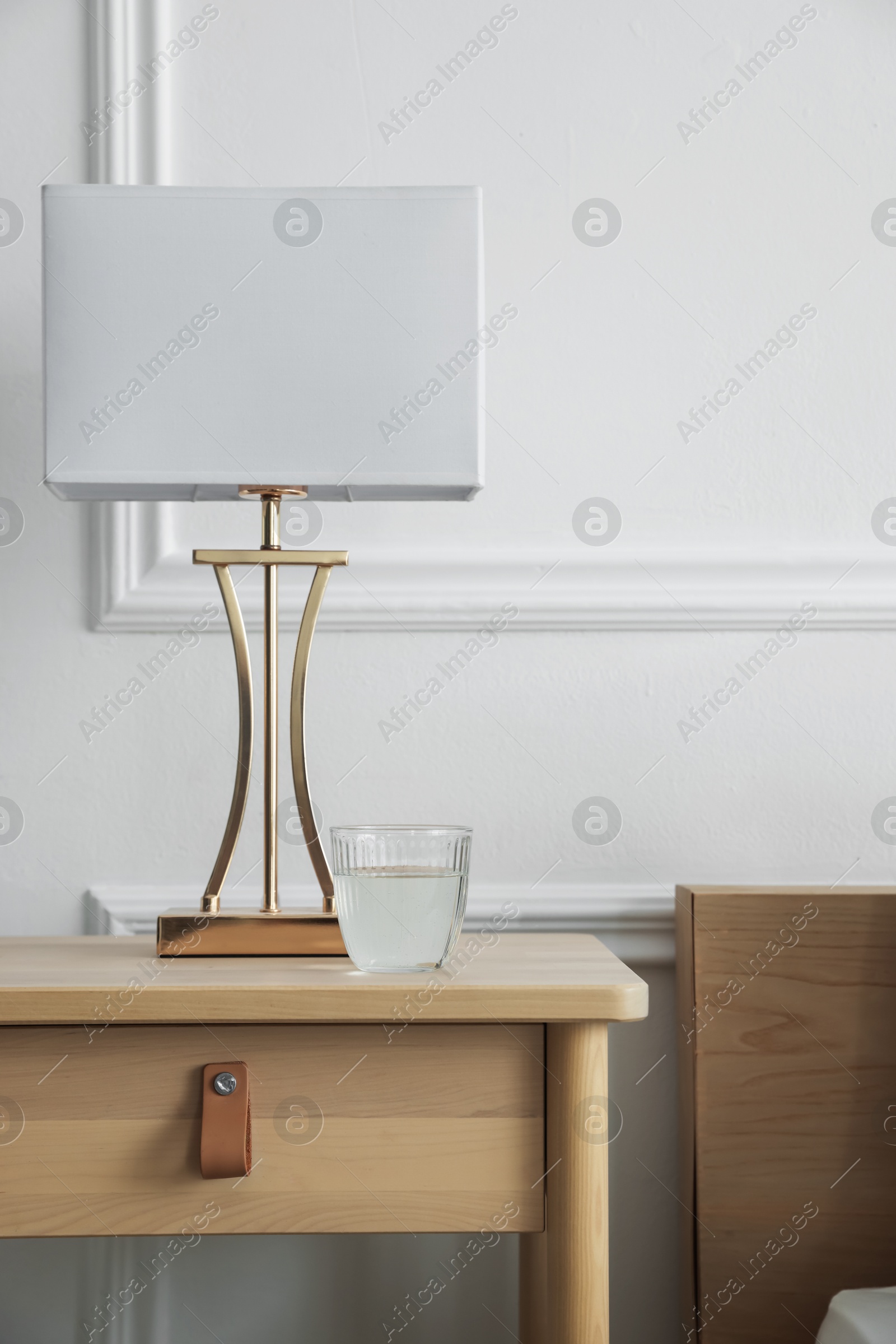 Photo of Bedside table with lamp and glass of water near bed indoors