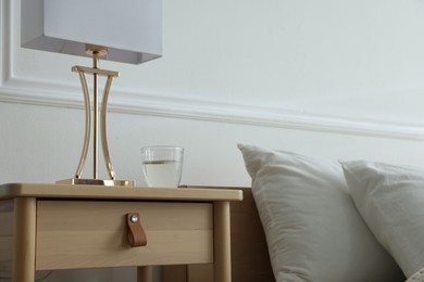 Photo of Bedside table with lamp and glass of water near bed indoors