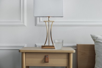 Photo of Bedside table with lamp and glass of water near bed indoors