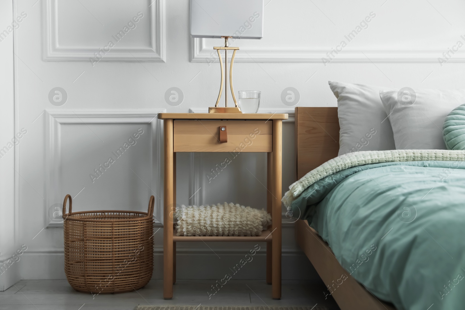 Photo of Bedside table with lamp and glass of water near bed indoors