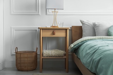 Photo of Bedside table with lamp and glass of water near bed indoors