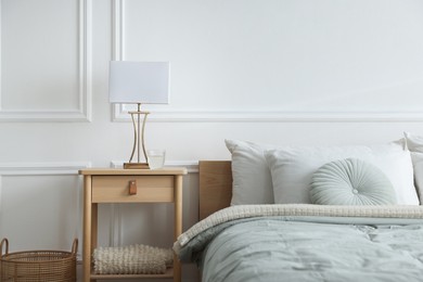 Photo of Bedside table with lamp and glass of water near bed indoors