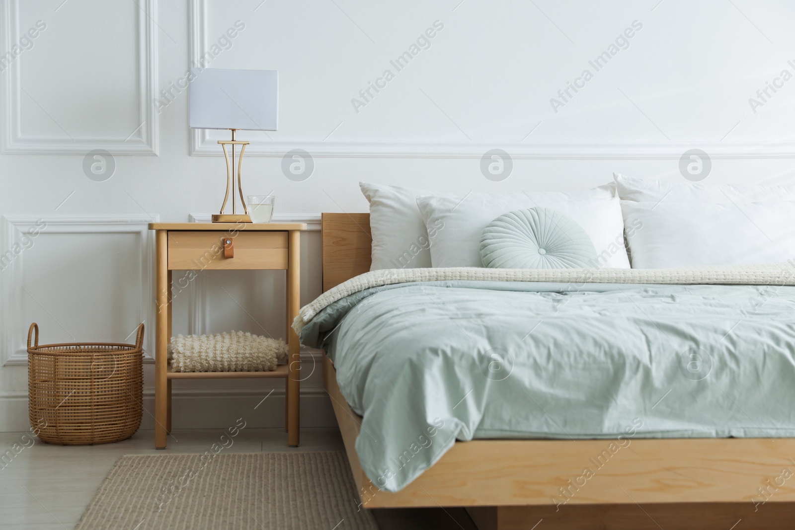 Photo of Bedside table with lamp and glass of water near bed indoors
