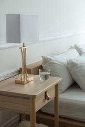 Photo of Bedside table with lamp and glass of water near bed indoors