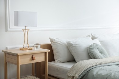 Photo of Bedside table with lamp and glass of water near bed indoors
