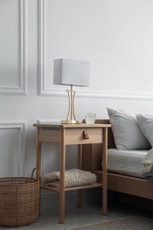 Photo of Bedside table with lamp and glass of water near bed indoors