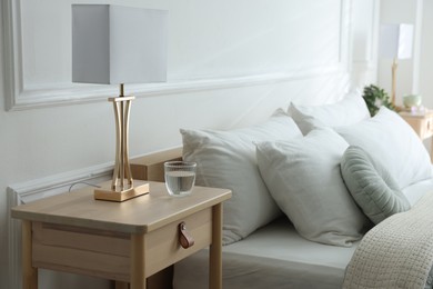 Photo of Bedside table with lamp and glass of water near bed indoors