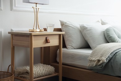 Photo of Bedside table with lamp and glass of water near bed indoors
