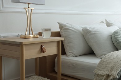Photo of Bedside table with lamp and glass of water near bed indoors