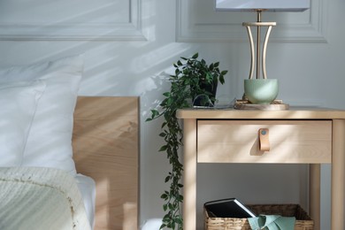 Photo of Bedside table with lamp and other decor near bed indoors