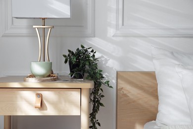 Photo of Bedside table with lamp and other decor near bed indoors