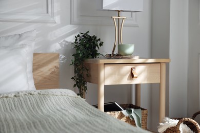 Photo of Bedside table with lamp and other decor near bed indoors