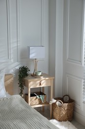 Photo of Bedside table with lamp and other decor near bed indoors
