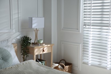 Photo of Bedside table with lamp and other decor near bed indoors