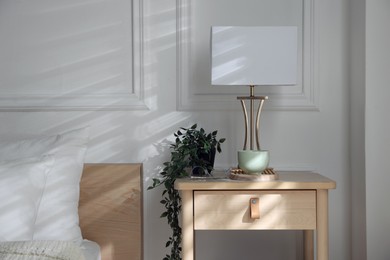 Photo of Bedside table with lamp and other decor near bed indoors