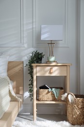 Photo of Bedside table with lamp and other decor near bed indoors