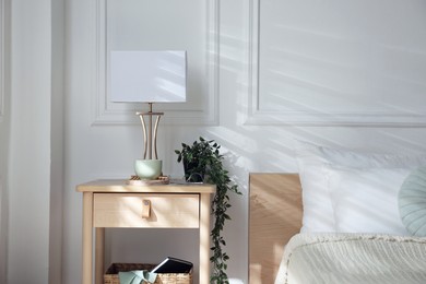 Photo of Bedside table with lamp and other decor near bed indoors