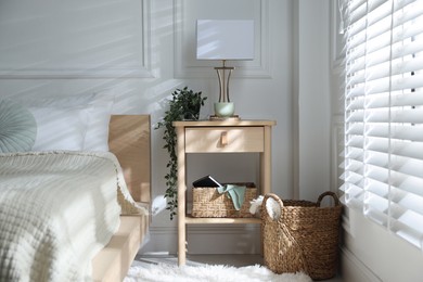 Photo of Bedside table with lamp and other decor near bed indoors