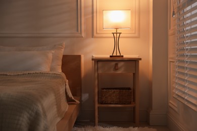 Photo of Bedside table with lamp near bed indoors