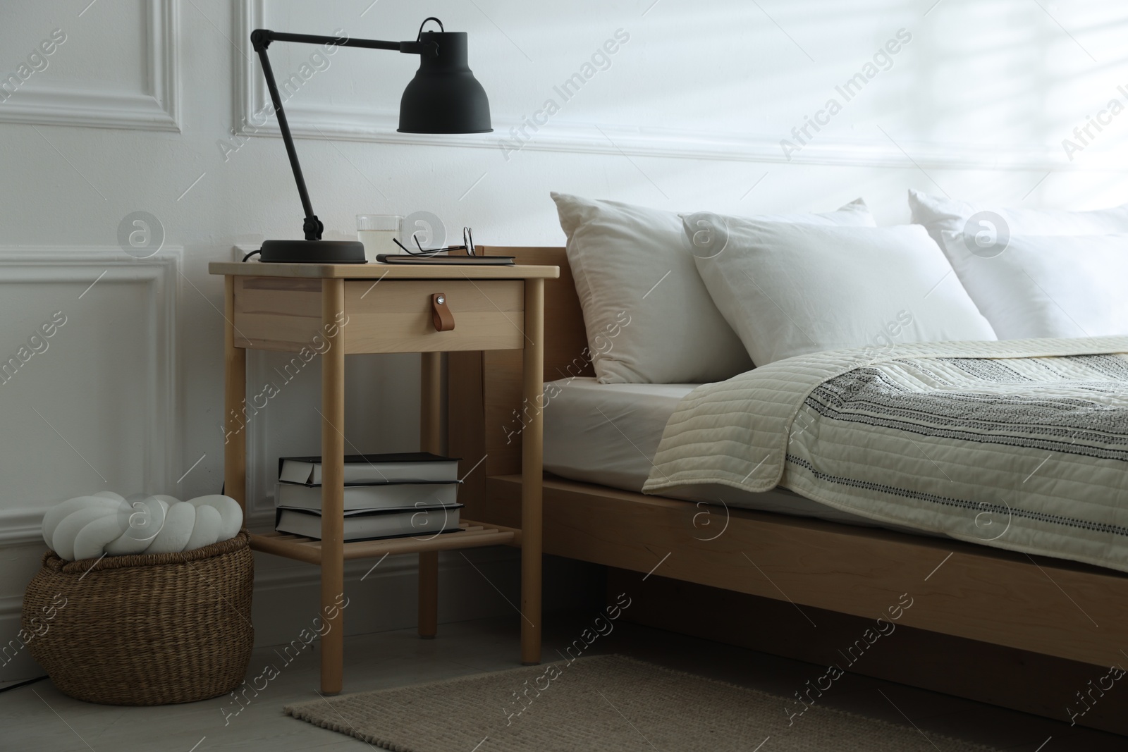 Photo of Bedside table with lamp, notebook, glasses, books and glass of water near bed indoors