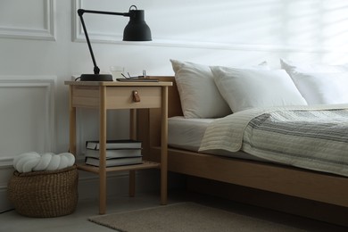 Photo of Bedside table with lamp, notebook, glasses, books and glass of water near bed indoors