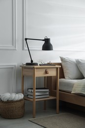 Photo of Bedside table with lamp, notebook, glasses, books and glass of water near bed indoors