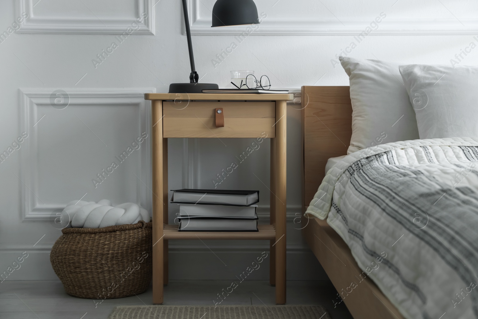 Photo of Bedside table with lamp, notebook, glasses, books and glass of water near bed indoors
