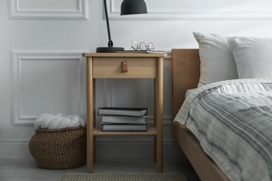 Photo of Bedside table with lamp, notebook, glasses, books and glass of water near bed indoors
